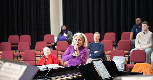 A woman sings into a microphone with audience members in the background. 